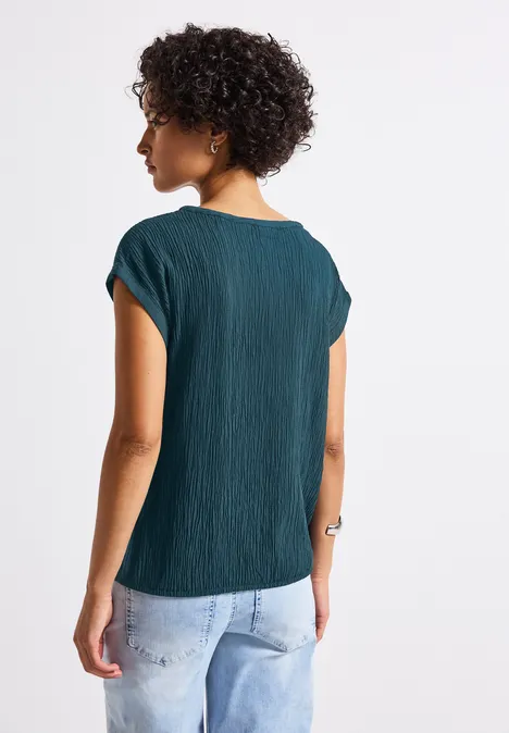 Frau mit lockigem Haar, grünem Oberteil und Jeans von hinten zu sehen.